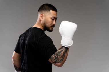 Beyaz boks eldiveni giymiş yakışıklı, ciddi bir Koreli boksörün portresi. Gri arka planda soyutlanmış bir şekilde başka tarafa bakıyor. Model