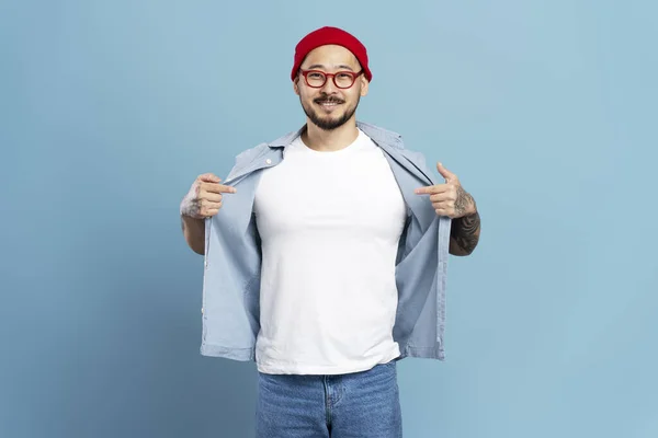 自信を持って笑顔のアジア人男性 赤い帽子をかぶったヒップスター スタイリッシュな眼鏡 青い背景で孤立した白いTシャツ モックアップ — ストック写真
