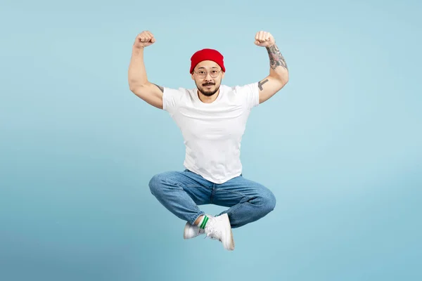 強いアジア人男性 スタイリッシュなタトゥーでボディービルダー 青い背景に隔離された筋肉を示しています ロタスポーズでハイジャンプする筋肉の韓国男性 カメラを見ます ジムワークアウト スポーツ 健康的なライフスタイル — ストック写真