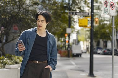 Sokakta mobil uygulama alışverişi yapan yakışıklı Asyalı bir adam akıllı telefon tutuyor. Genç hippi erkek sohbeti, kısa mesaj, internet iletişimi. Teknoloji, mobil bankacılık.