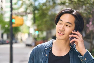 Yakışıklı, gülümseyen Asyalı bir adamın cep telefonuyla konuşan, caddeye bakan, fotokopi çeken bir portresi. Teknoloji konsepti 
