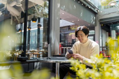 Gülümseyen, yakışıklı Asyalı yönetici çalışıyor, akıllı telefon kullanıyor, modern kafede internette geziniyor, uzaktan çalışıyor. Cep telefonu sohbeti yapan genç Japon öğrenci. İnternet iletişimi