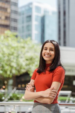 Mutlu Hintli kadının dikey görüntüsü dişlek gülümsemesiyle kameraya bakıyor, kollarını caddede kavuşturuyor. Çekici Asyalı model resimler için poz veriyor. Pozitif yaşam tarzı, doğal güzellik. 