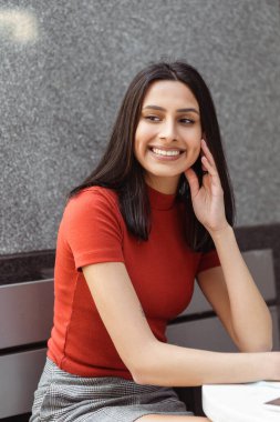 Güzel gülümseyen Hintli bir kadının dikey portresi şık günlük kıyafetler giyip sokağa bakıyor. Üniversite kampüsünde oturan esmer, sevimli Asyalı öğrenci. Eğitim kavramı 