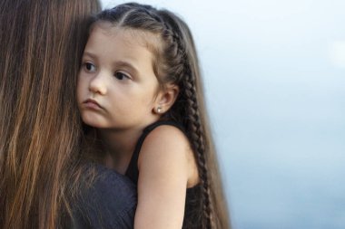 Sakin küçük kız tatilini okyanus sahilinde geçirirken annesine sarılıyor. Aile ilişkileri kavramı