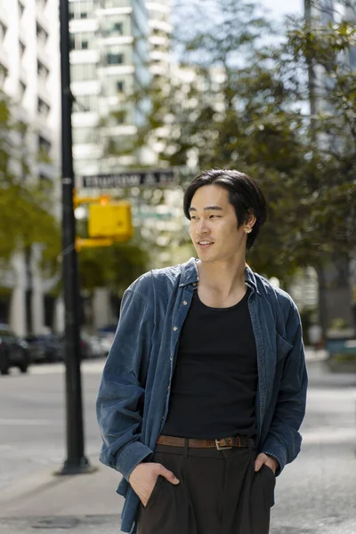 一个迷人的笑着的亚裔男子的画像 他手插在口袋里 穿着时髦的休闲装 站在街上遥望远方 — 图库照片