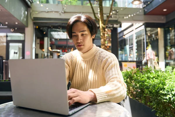 Confident asian man author typing laptop computer keyboard, sitting outdoor cafe. Successful Japanese programmer at workplace. Technology concept