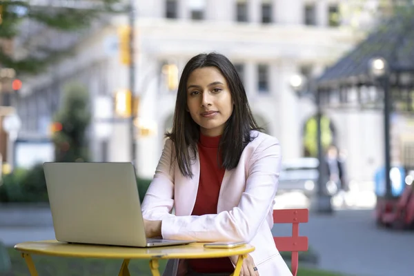 Portrait of young confident Indian businesswoman, freelancer using laptop computer looking at camera, working online sitting at workplace. Successful business