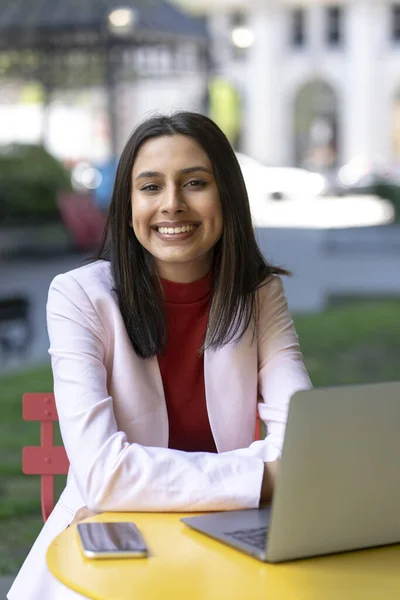 Portrait of smart smiling Indian student studying, using laptop, sitting in university campus, education concept. Successful asian businesswoman, young freelancer working online looking at camera