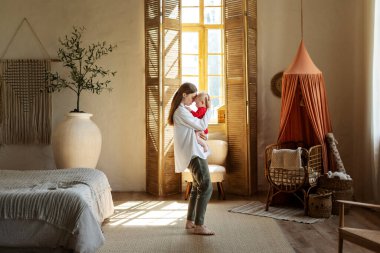 Güzel, gülümseyen genç bir anne kucağında, tatlı küçük bebeğiyle evde oynuyor, eğleniyor. Aşk, ilgi, annelik kavramı 