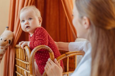 Genç, gülümseyen bebek bakıcısı evde bebek yatağında küçük bebekle iletişim kuruyor. Mutlu aile birlikte. İlk adım, bebek gelişimi konsepti 