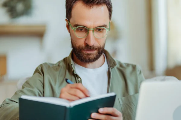 英俊的大胡子商人戴着眼镜记笔记 在家里学习 聪明的学生学习语言 在线教育概念 — 图库照片