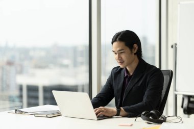 Yakışıklı Asyalı işadamının portresi, başarılı bir tüccar dizüstü bilgisayar kullanıyor, evden internet üzerinden çalışıyor. Freelancer metin yazarı klavyede yazı yazıyor, proje planlama işyerinde oturuyor. Teknoloji