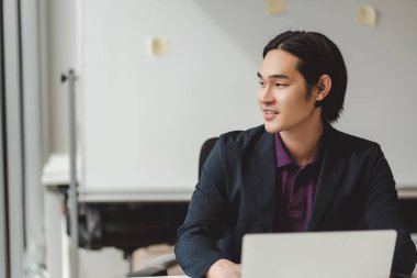 Resmi kıyafet giymiş gülümseyen Asyalı adamın portresi, iş yerinde çalışmak, dizüstü bilgisayar kullanmak. Profesyonel metin yazarı klavyede yazı yazıyor, başka tarafa bakıyor. İş konsepti