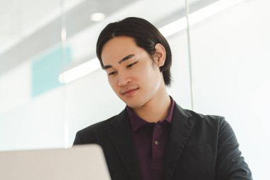 Bilgisayarı kullanan Asyalı bir adamın yakın plan portresi. İnternette çalışıyor, modern ofiste bir proje planlıyor. İş yerindeki akıllı işadamı, teknoloji sektörü konsepti