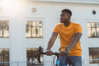 Yakışıklı, Afro-Amerikan bir adam, şehir caddesinde bisiklet sürüyor ve başka tarafa bakıyor. Spor, hobi, aktif yaşam tarzı konsepti 