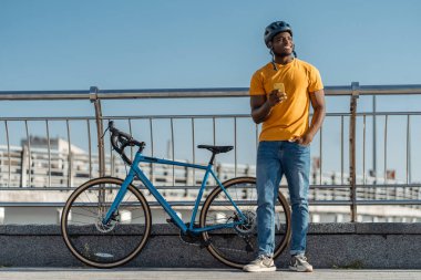 Sokakta bisiklet yanında duran kasklı, cep telefonu tutan gülümseyen Afrikalı bir adamın portresi. Yakışıklı sürücü e-postayı kontrol ediyor, online alışveriş. Teknoloji konsepti