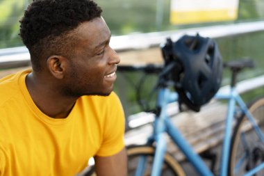 Gülümseyen Afro-Amerikan adam bisiklet sürdükten sonra bisikletle caddede dinlenirken gözlerini kaçırıyor. Halk yaşam tarzı konsepti