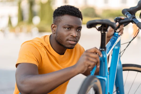 stock image Portrait of handsome attractive african american man repairing bicycle, looking at seat. Young guy preparing. Concept of cycling, travel