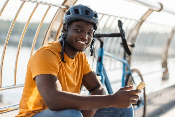 Szczęśliwy Wielorasowy Mężczyzna Kasku Ochronnym Patrząc Kamerę Trzymając Telefon Komórkowy — Zdjęcie stockowe