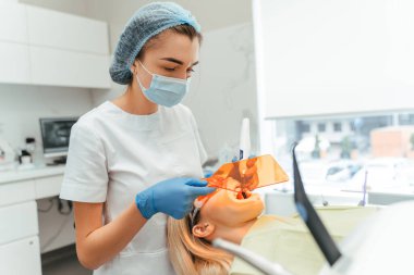 Koruyucu maskeli kadın dişçi, dişçi kliniğinde kadın hasta için dolgu yapıyor. Modern diş sağlığı kliniği kavramında diş tedavisi