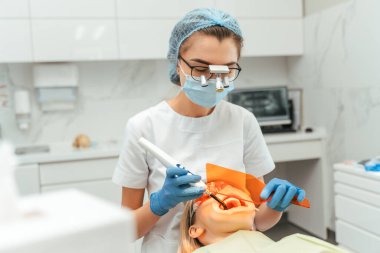 Klinikte dişçisi olan bir kadın hasta. Kadın doktor ultraviyole ışıkla diş beyazlatma prosedürü uyguluyor. Diş beyazlatma kavramı