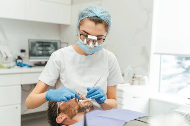 Diş kliniğinde oturup dişlerini kontrol eden orta yaşlı, sakallı bir hasta. Somatoloji kavramı 