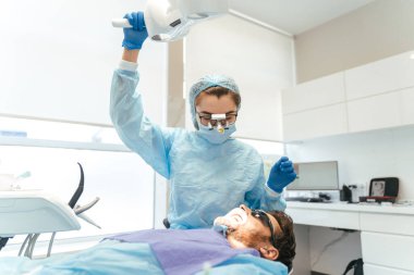 Kafasında mikroskop olan kadın cerrah erkek hasta için diş ameliyatı yapıyor. Kliniğe diş implantı ya da diş çıkarma kurulumu. Ortodonti ameliyatı sırasında genel anestezi. 