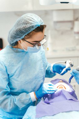 Kafasında mikroskop olan kadın cerrah erkek hasta için diş ameliyatı yapıyor. Kliniğe diş implantı ya da diş çıkarma kurulumu. Ortodonti ameliyatı sırasında genel anestezi. 