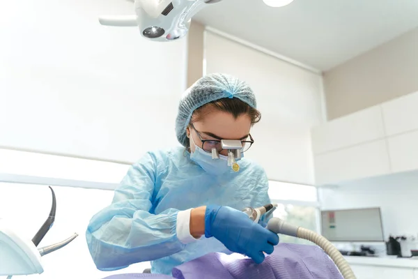 Koruyucu elbiseli kadın diş hekimi, diş hekimindeki erkek hastaya profesyonel diş temizliği yapıyor. Sağlık konsepti için diş bakımı 
