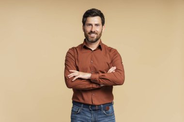 Yakışıklı gülümseyen orta yaşlı iş adamı, menajer kollarını çapraz olarak bej arka planda tutuyor. Başarılı iş konsepti 