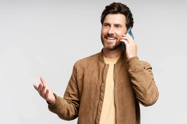 皮のジャケットのハンサムな笑顔の男のウエストアップの肖像画 携帯電話で話しながらジェスチャー 灰色の背景の上に孤立 コミュニケーションのコンセプト — ストック写真