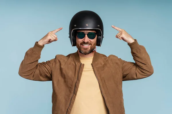 ハンサムな笑顔の男の肖像画 サングラスを身に着けているバイカー 青い背景に隔離されたヘルメットの指を指します 交通コンセプト — ストック写真
