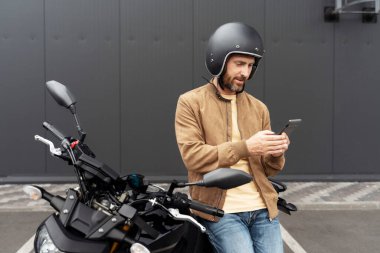 Kendine güvenen şık bir adam, kask takan motorcu cep telefonu kullanıyor spor motosikletinin yanında duruyor. Güzel bir manken, şık bir deri ceket giyiyor. Motosikletli resimlere poz veriyor. 