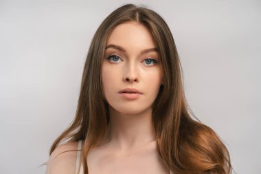 Gri arka planda izole edilmiş kameraya bakan uzun, güzel saçlı genç bir kadının portresi. Çekici kadın, model stüdyoda poz veriyor. 