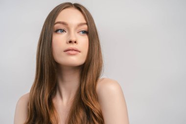 Gri arka plan fotokopi alanında izole edilmiş, uzun, güzel saçlı genç bir kadının portresi. Çekici kadın, model stüdyoda poz veriyor. 