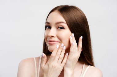 Gri arka planda izole edilmiş, güzel, uzun saçlı, kameraya bakan ve birbirine dokunan bir kadının portresi. Doğal güzellik, cilt bakımı