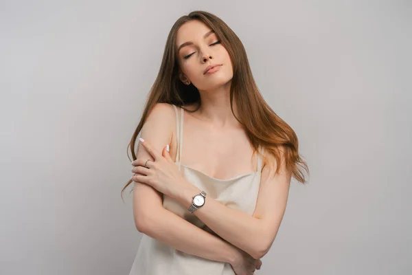 Portrait of cute woman hugging herself with watch on her hand isolated on gray background. Beautiful female wearing beautiful nightgown posing in studio with closed eyes. ?oncept of sexuality