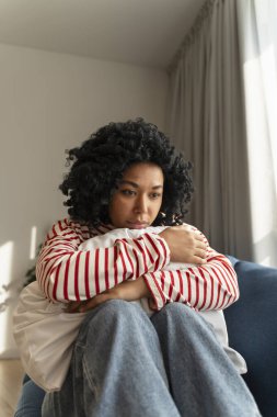 Mutsuz Afrikalı Amerikalı kadın yastığını kucaklıyor evde tek başına oturuyor. Depresyon kavramı 