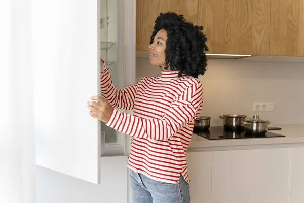 スタイリッシュなモダンなキッチンで冷蔵庫を開く美しく魅力的なアフリカ系アメリカ人女性 家庭電化製品を使用している主婦 機器のコンセプト — ストック写真