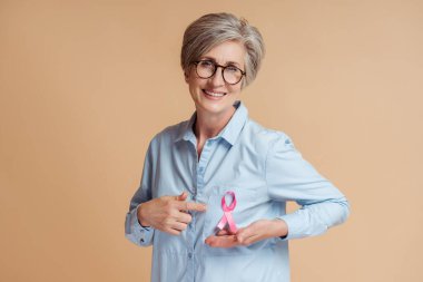 Arka planda pembe kurdele gösteren gülümseyen son sınıf öğrencisi kadın. Göğüs kanseri farkındalığı ayı