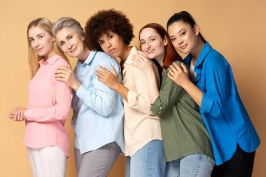 Bir grup güzel, gülümseyen, çok ırklı kadın bej arka planda gömlek giyiyor.