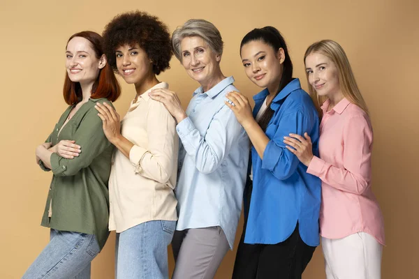 Bir grup güzel, güler yüzlü, çok kültürlü kadın şık gömlekler giyip birbirlerine sarılıyorlar.