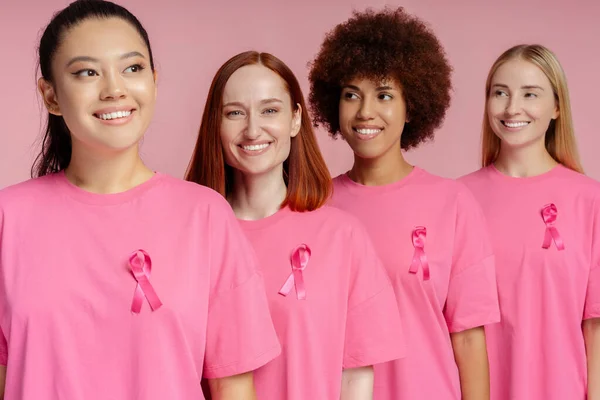 Smiling multiracial women with pink ribbon isolated on pink background. Breast cancer awareness