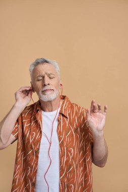 Beyaz, yaşlı, gri sakallı, şık kıyafetleri olan, kulaklıkla rahatlatıcı müzik dinleyen, gözleri kapalı, izole edilmiş bej arka planda dinlenen bir adam. - İnsanlar. Eğlence. Yaşam biçimi