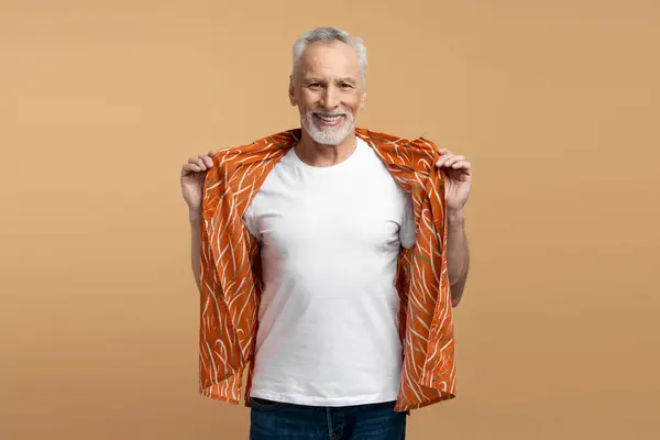 英俊的 面带微笑的灰发老人的画像 穿着时髦的橙色衬衫和白色T恤 背景与米黄色格格不入 积极的生活方式 夏天的概念 — 图库照片