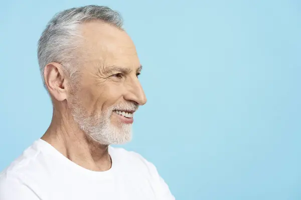 身着白色T恤的老人面带微笑 穿着蓝色背景的白色T恤 复制空间 脸型轮廓 迷人的退休人员在演播室摆姿势拍照 牙科护理概念 — 图库照片