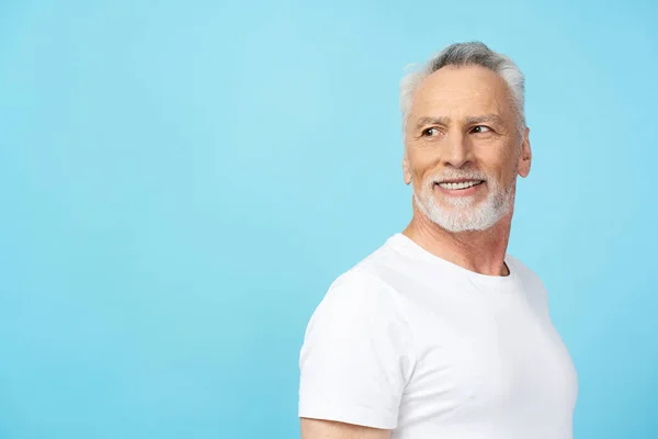 服装肖像吸引人的灰色头发男人穿着白色的T恤 看起来与蓝色背景隔离 复制空间 微笑着自信的资深男士们在演播室里摆姿势拍照 保健概念 — 图库照片