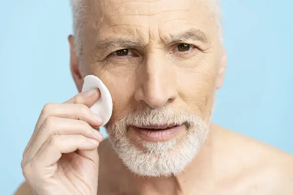 Closeup Serious Senior Man Removing Makeup Cotton Sponge Isolated Blue — Stock Photo, Image