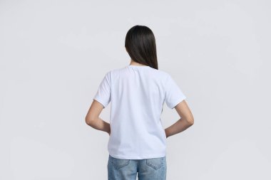 İnce, koyu renk saçlı genç bir kadının arka görünüşü, beyaz, boş tişörtlü bir genç kız, beyaz izole arka planda kamera karşısında dikiliyor. Reklam metni için alanı kopyala